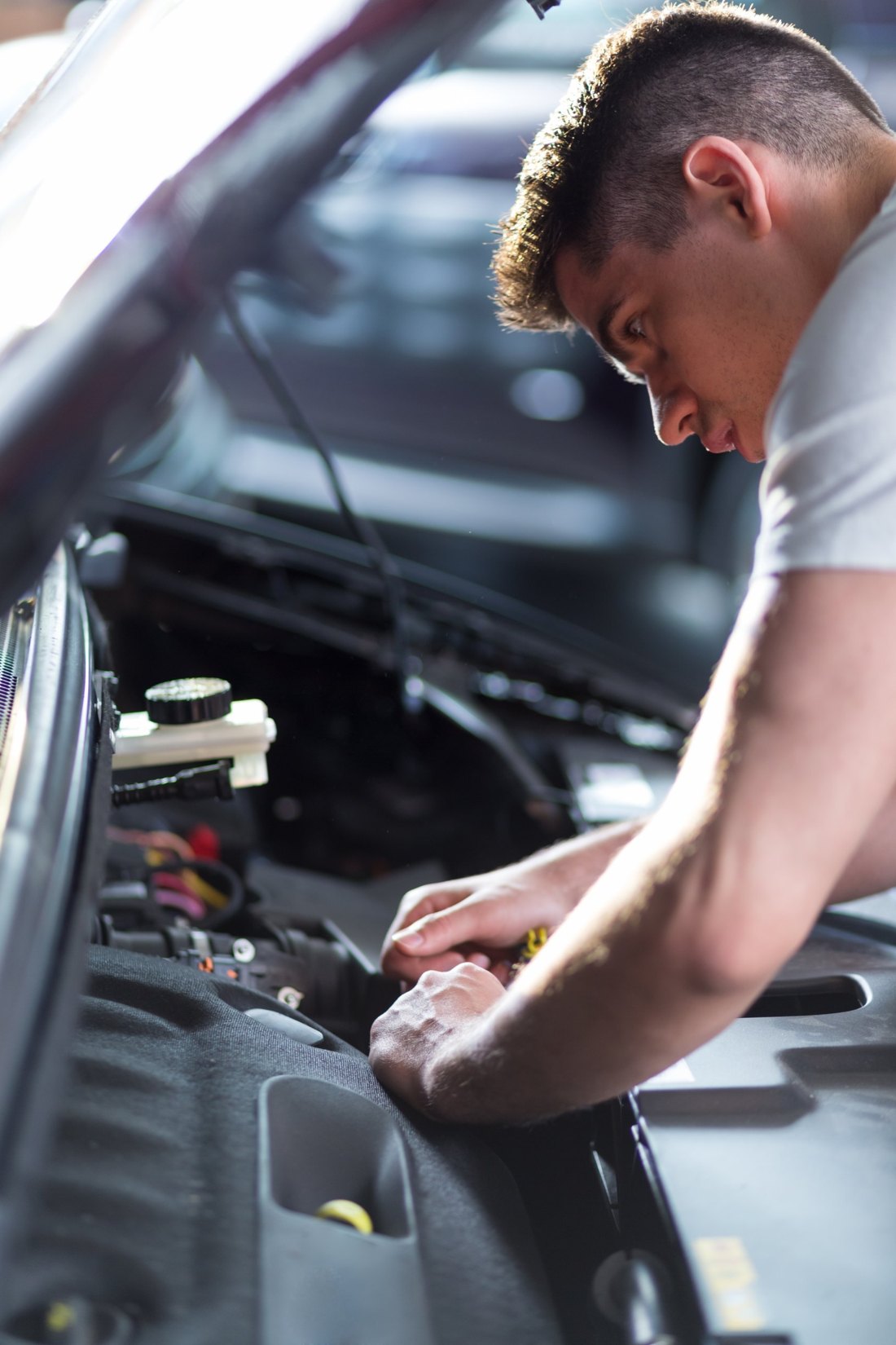 A young man leaning over a car engine, working with a tool